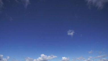 Beyaz kabarık bulutların dinamik hareketlerini gösteren büyüleyici gerçek zamanlı bir zaman dilimi videosu derin mavi gökyüzünde, atmosferik koşulların huzurlu ve geçici doğasını gösteriyor..
