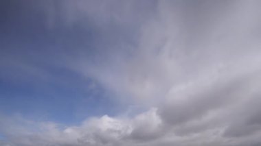 Parlak mavi gökyüzünde hızla sürüklenen dinamik beyaz bulutları gösteren büyüleyici bir zaman dilimi videosu, gerçek zamanlı olarak doğal hareket ve atmosferik değişimleri gösteriyor..