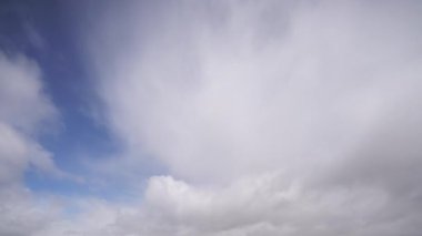Bulutların zaman çizelgesi dinamik bir şekilde açık mavi gökyüzünde hareket ederek, gökyüzünün dingin ama değişen doğasını yakalıyor..