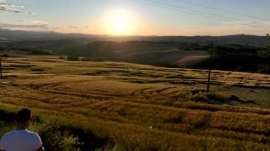 İtalya 'nın Marche kentindeki buğday tarlalarının üzerinde, hareketsiz duran ve gün batımını seyreden bir insanın altın saat görüntüsü. Sıcak ışık, doğal güzellik ve huzurlu atmosfer.
