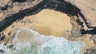 Tindaya, Fuerteventura, İspanya 'da bulunan Playa Tebeto' daki sakin plajın keyfini çıkarırken kuma uzanmış bir kadının insansız hava aracı görüntüsü.