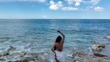 Bir kadın İtalya 'nın Marche kentinde kayalık bir sahilde denize bakıyor. Çekim, geniş okyanusu, mavi gökyüzünü ve Adriyatik kıyılarının barışçıl atmosferini yakalıyor.