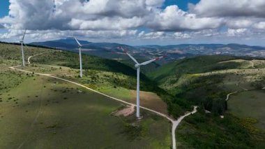 İtalya 'nın Marche bölgesindeki kayan tepelerdeki görkemli rüzgar türbinlerinin hava manzarası yemyeşil ve dramatik bir gökyüzü ile doğal güzelliğin ortasında yenilenebilir enerjiyi vurguluyor.