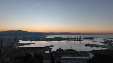 İtalya 'nın Marche bölgesindeki Ancona limanında sakin bir günbatımı, renkli gökyüzüne karşı siluetler ve vinç ve gemilerle, sükunet ve güzelliği yansıtıyor.