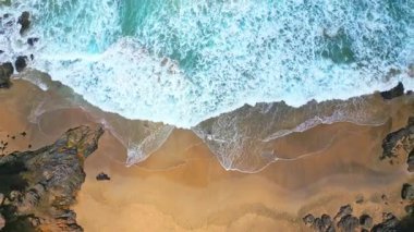 Kanarya Adaları, Fuerteventura, İspanya 'daki Tindaya Sahili' nin kumlu kayalık sahillerinde dalgalı denizde yürüyen bir kadının uzaktan kumandalı hava aracı görüntüsü. Kıyı şeridi dalgalı mavi bir okyanusa karşı engebeli uçurumlara sahiptir..