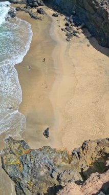 İspanya, Fuerteventura 'daki Tindaya Sahili' nin kumlu ve kayalık sahillerinde yürüyen bir kadının en iyi hava aracı görüntüsü. Kıyı şeridi dalgalı mavi bir okyanusa karşı engebeli uçurumlara sahiptir..