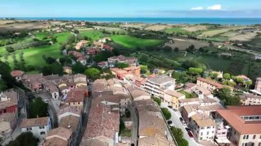 Çevresi yeşil tepeler, tarım arazileri ve deniz manzaralarıyla çevrili canlı bir İtalyan köyünün insansız hava aracı videosu. Gündüz yakalanan, resimli evler, ağaçlar ve Akdeniz manzarasıyla