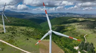 İtalya 'nın Marche bölgesinin yemyeşil tepelerindeki rüzgar türbinlerinin hava manzarası. Yuvarlanan manzaralar, kabarık bulutlarla benekli bir gökyüzünün altında yenilenebilir enerjiyle buluşur.