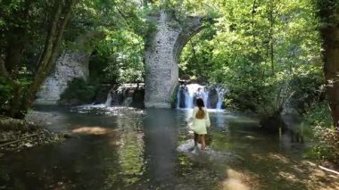 İtalya 'nın Marche bölgesinde çağlayan şelaleler ve yemyeşil sularla dolu tarihi bir taş köprünün altındaki sakin bir nehirde yürüyen bir kadın bir macera ve huzur anı yakalıyor.
