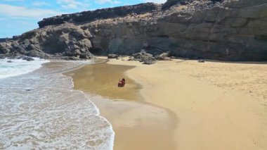 Sahilde renkli bikinili bir kadın tatiller sırasında Fuerteventura, Kanarya Adaları 'ndaki Tindaya Sahili' nde mutlu bir şekilde oynuyor. Kıyı şeridi dalgalı mavi bir okyanusa karşı engebeli uçurumlara sahiptir..