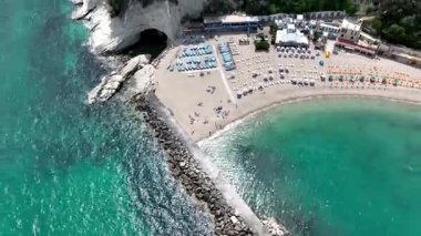 İtalya 'nın Marche bölgesinde güzel bir sahil manzarası, turkuaz sular, kumlu kıyılar ve renkli şemsiyeler sergileniyor. Manzara dramatik uçurumlar ve yemyeşil