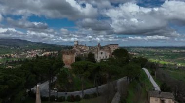 İtalya 'nın Treia kentindeki ortaçağ köyünün havadan görünüşü, antik kuleleri, taş binaları ve bulutlu dramatik bir gökyüzünün altında yuvarlanan yeşil tepeleri gösteriyor.