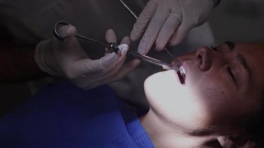 Bir diş hekimi titiz bir diş temizleme prosedürünü iyi aydınlatılmış bir klinikte, hasta için optimum ağız temizliği sağlayan özel aletler kullanarak gerçekleştirir.