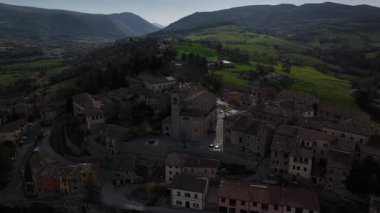 İtalya, Belforte del Chienti 'nin hava manzarası, sıcak günbatımı ışığında yıkandı. Ortaçağ köyü, arka planda dramatik dağ manzaralı yeşil tepelerin arasına kurulmuştur.
