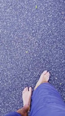 Bir insan, Melbourne, Victoria, Avustralya 'da asfalt bir yolda yalınayak yürüyor, dağınık yapraklarla, sakin ve doğal bir kentsel yürüyüş sahnesi yaratıyor..