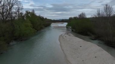 Yoğun orman ve kumsallarda süzülen sakin bir İtalyan nehrinin havadan görünüşü, üzerinden geçen bir köprü ve karamsar bahar gökyüzü doğal güzelliği artırıyor.