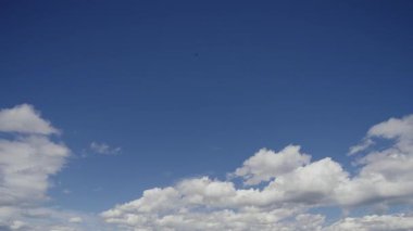 Beyaz kabarık bulutların dinamik hareketlerini gösteren büyüleyici gerçek zamanlı bir zaman dilimi videosu derin mavi gökyüzünde, atmosferik koşulların huzurlu ve geçici doğasını gösteriyor..