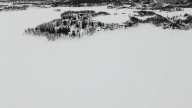 Norveç 'teki el değmemiş karlı bir arazinin insansız hava aracı görüntüsü, kar dolu ormanlar ve uzak dağlarla çevrili geleneksel İskandinav evlerinin görüntüsü..