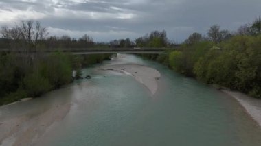 Yoğun orman ve kumsallarda süzülen sakin bir İtalyan nehrinin havadan görünüşü, üzerinden geçen bir köprü ve karamsar bahar gökyüzü doğal güzelliği artırıyor.