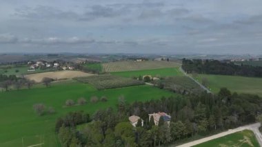 Yeşil tarlalar, üzüm bağları, zeytin bahçeleri, dolambaçlı yollar ve yumuşak bir gökyüzünün altındaki yuvarlanan tepelerin arasına yerleştirilmiş geleneksel çiftlik evleri içeren İtalyan kırsal bölgelerinin geniş hava manzaraları.