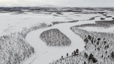İsveç 'in Kiruna kenti yakınlarındaki geniş karlı araziyi gösteren hava aracı videosu. Görüntüler, yoğun, karlı ağaçlar ve dolambaçlı kar yollarıyla karla kaplı geniş bir alanı gösteriyor. Huzurlu ve izole bir kış manzarası sunuyor.