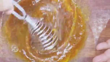 Bir kadının ellerinin cam bir kasede çırpılmış malzemelerle karıştırdığı, ahşap bir tezgahta kurabiye hamuru hazırlayan, ev yapımı pişirmenin keyfini somutlaştıran yakın çekim görüntüsü.