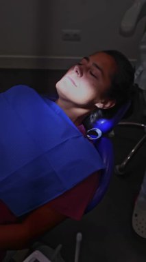 Hasta dişçi koltuğunda rahatlamış, profesyonel diş temizleme prosedürüne hazır. Diş muayenehanesi ayarları ağız sağlığı ve düzenli kontrollerin önemini vurgular