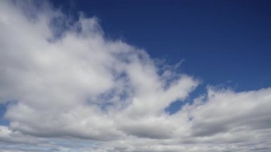 Geniş açılı zaman dilimi video görüntüsü gökyüzündeki dinamikleri gösteriyor kabarık bulutlar canlı, mavi bir zemin üzerinde süzülüyor, nefes alan gökyüzünün doğal hareketini çağrıştırıyor.