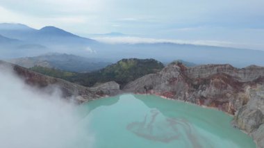 Doğu Java, Endonezya 'daki İjen volkanının engebeli araziyle çevrili ve volkanik gazlarla kaplı canlı, asitli krater gölünü gösteren ve dinamik doğal aktiviteyi gösteren insansız hava aracı görüntüsü..