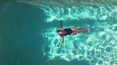 Bir kadın yüzme havuzunda huzur içinde yüzerken görülüyor. Güneşin altında güneşlenerek, bir mayo giyiyor, dingin ve rahatlatıcı bir yaz havası yayıyor. Su güneş ışığını yansıtır.