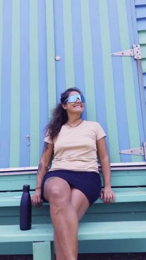 Brighton Beach, Melbourne 'da canlı Brighton Banyo Kutuları' nın önünde rahatça oturan bir kadın. İkonik arkaplan ve güneşli gün sahilin cazibesini vurguluyor