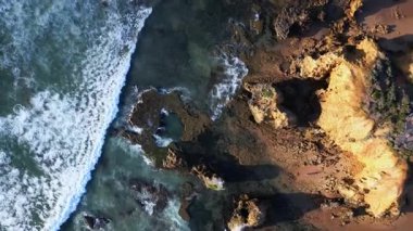 Büyüleyici bir hava manzarası Avustralya 'daki Büyük Okyanus Yolu boyunca uzanan engebeli kıyı şeridini yakalar. Dalgalar kayalık kıyıya çarpıyor, bu ünlü yolun doğal güzelliğini vurguluyor..