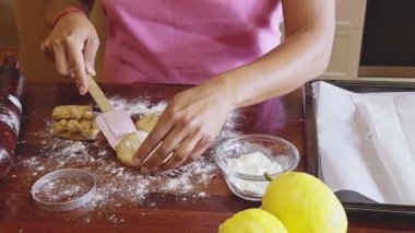 Pembe önlüklü bir kadın, ahşap bir tezgahta, un ve limonla çevrili kurabiye hamurunu ustalıkla hazırlar. Sıcak bir mutfakta ev yapımı zevki somutlaştırır.