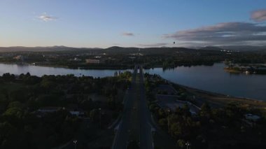 İnsansız hava aracı görüntüleri Canberra, Avustralya 'da geniş manzaralar, sakin göl, Parlamento Binası ve hareketli bir yol sergilerken görülüyor. Görüntü gerçek zamanlı olarak sakin ve manzaralı titreşimler yayar..