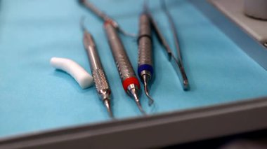 Diş temizliği için kullanılan diş aletlerinin yakın plan bir resmi, bir tepsiye yerleştirilmiş, hijyenik mavi bir çarşaf ile. Klinik ortamda ağız sağlığını korumak için gerekli aletler.