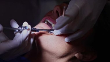 Bir diş hekimi, bir hastaya diş temizleme prosedürü uygulamak için özel aletler kullanır ve klinik ortamda oral sağlık sağlar.