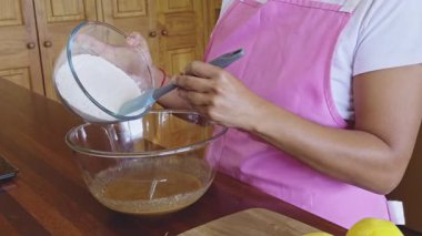 Pembe önlüklü bir kadın sıcak bir mutfakta ev yapımı kurabiye yapmak için malzemeleri karıştırıyor. Sahne, sıcak ve davetkar pişirme sürecini özenle ve titizlikle yakalar.