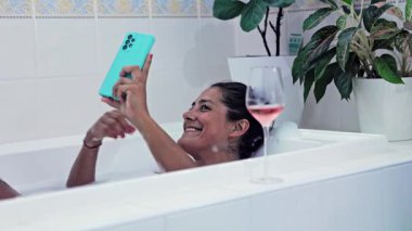 Bir kadın küvette dinleniyor, elinde akıllı bir telefonla selfie çekiyor ve bir öpücük yolluyor, yanında bir bardak gül şarabı ile; hareket gerçek zamanlı olarak yakalanıyor..