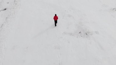 İsveç, Kiruna 'da bir İHA tarafından yakalanan, kar üzerinde yürüyen, kırmızı ceketli, tanınmayan bir kişinin üst hava görüntüsü. Görüntü ayak seslerini ve sakin kış manzarasını gösteriyor..