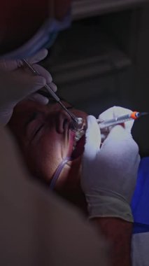 Eldivenler konusunda uzman bir diş hekimi diş temizleme prosedürü uygulamak için özel aletler kullanır, plağın çıkarılması ve sağlıklı, temiz dişler için ağız hijyeninin sağlanması üzerine odaklanır.