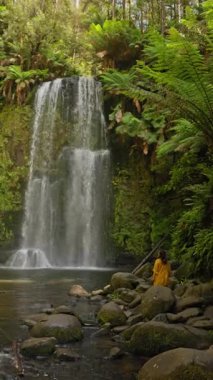 Avustralya 'nın ünlü Büyük Okyanus Yolu boyunca uzanan yemyeşil bir ormanda serin çağlayan şelaleler. Sarılı bir kadın doğal güzelliğe ve sükunete hayran..