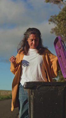 Bir kadın, güneşli bir günde çöpü dışarı çıkararak ev atıklarıyla uğraşır. Burnunu tutuyor ve atık yönetimindeki günlük rutinlerin ortak bir yönünü gösteriyor.