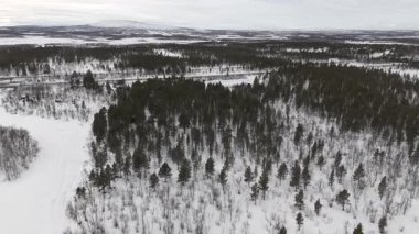 İHA görüntülerinde geniş kar örtülü manzaralar, yoğun ormanlar ve İsveç 'in Kiruna kenti yakınlarında asfalt bir otoyol görülüyor ve yukarıdan gerçek zamanlı bir kış manzarası görülüyor..