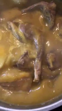 Kalın, sarı bir sosta kaynayan tavşan etinin yakın çekimi. İhale kesimleri yavaş yavaş pişiyor ve geleneksel ev mutfağının özünü yakalıyor.