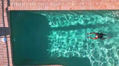 Bir kadın, sakin bir havuzda dinlenirken, sakin bir anı yakalar. Açık mavi su güneş ışığını yansıtarak davetkar ve barışçıl bir atmosfer yaratır.