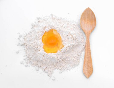 Ahşap bir kaşık, un yığınına yerleştirilmiş çiğ bir yumurtanın yanında duruyor ve klasik pişirme malzemelerini sergiliyor. Tarifler, yemek pişirme ve pişirme kavramları için mükemmel.