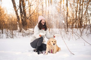 Neşeli bir kadın kış ormanında köpeğinin yanında karla oynar. O sıcak pembe bir şapka ve ceket giyer, karlı manzara ve çıplak ağaçlar onları sararken sakin bir ortamda.