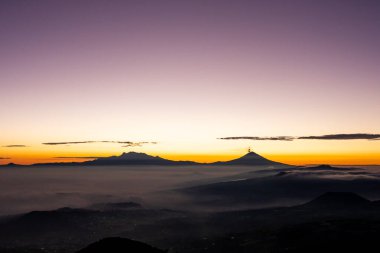 Sisli dağların üzerinden sersemletici bir gün doğumu, canlı bir gökyüzüne karşı dağların siluetlerini aydınlatıyor. Bulutlar ve ışıldayan ufuklarla sakin bir sahne..