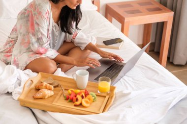 Sabahları rahat bir yatakta, nefis bir kahvaltıyla tepsinin yanında otururken, uyurgezer dizüstü bilgisayarda tanınamayan bir kadın.