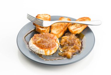 Zarif keçi peynirli rulo üstü ihtişamlı karamelize soğanla kaplanmış, klas siyah bir tabakta altın-kahverengi ekmek dilimleriyle servis edilmiş, gurme iştah açıcı bir lezzet sunuyor